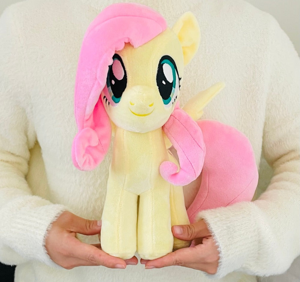Plush toy resembling a character with pink hair and a pink bow held by a person wearing a white sweater.