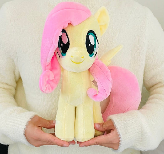Plush toy resembling a character with pink hair and a pink bow held by a person wearing a white sweater.