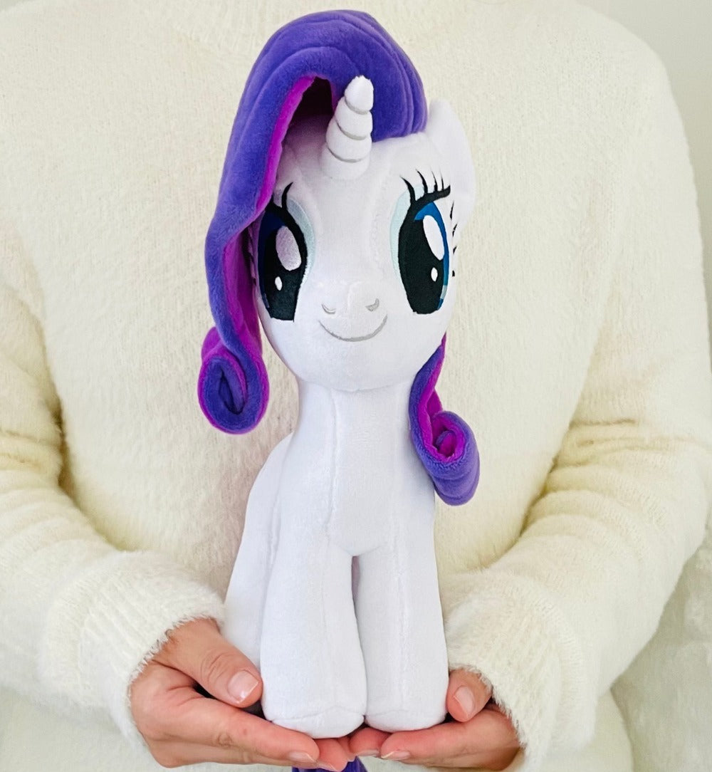 Plush toy unicorn with purple hair held by a person wearing a white sweater.