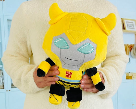 Person holding a yellow and gray plush toy with a Transformers logo.