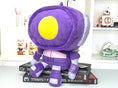 Load image into Gallery viewer, Purple and yellow plush toy on top of a book with shelves in the background