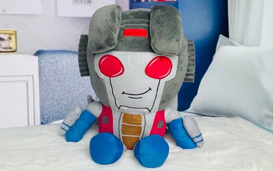Plush toy robot with red eyes and blue accents on a bed