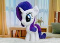 Load image into Gallery viewer, Plush toy unicorn with purple hair and tail in a room with curtains and books.
