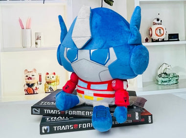Load image into Gallery viewer, Blue and gray plush toy on top of Transformers books with shelves in the background