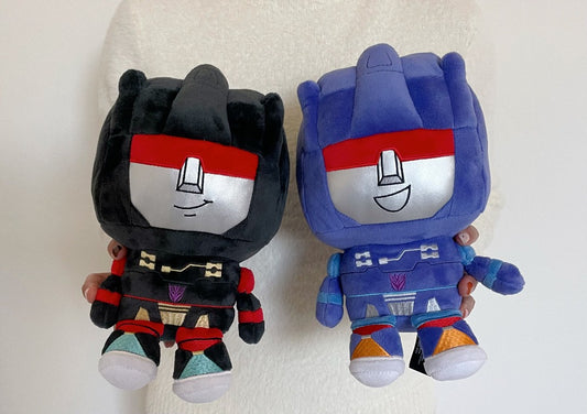 Two plush toys, one black and red, the other blue and red, on a light background.