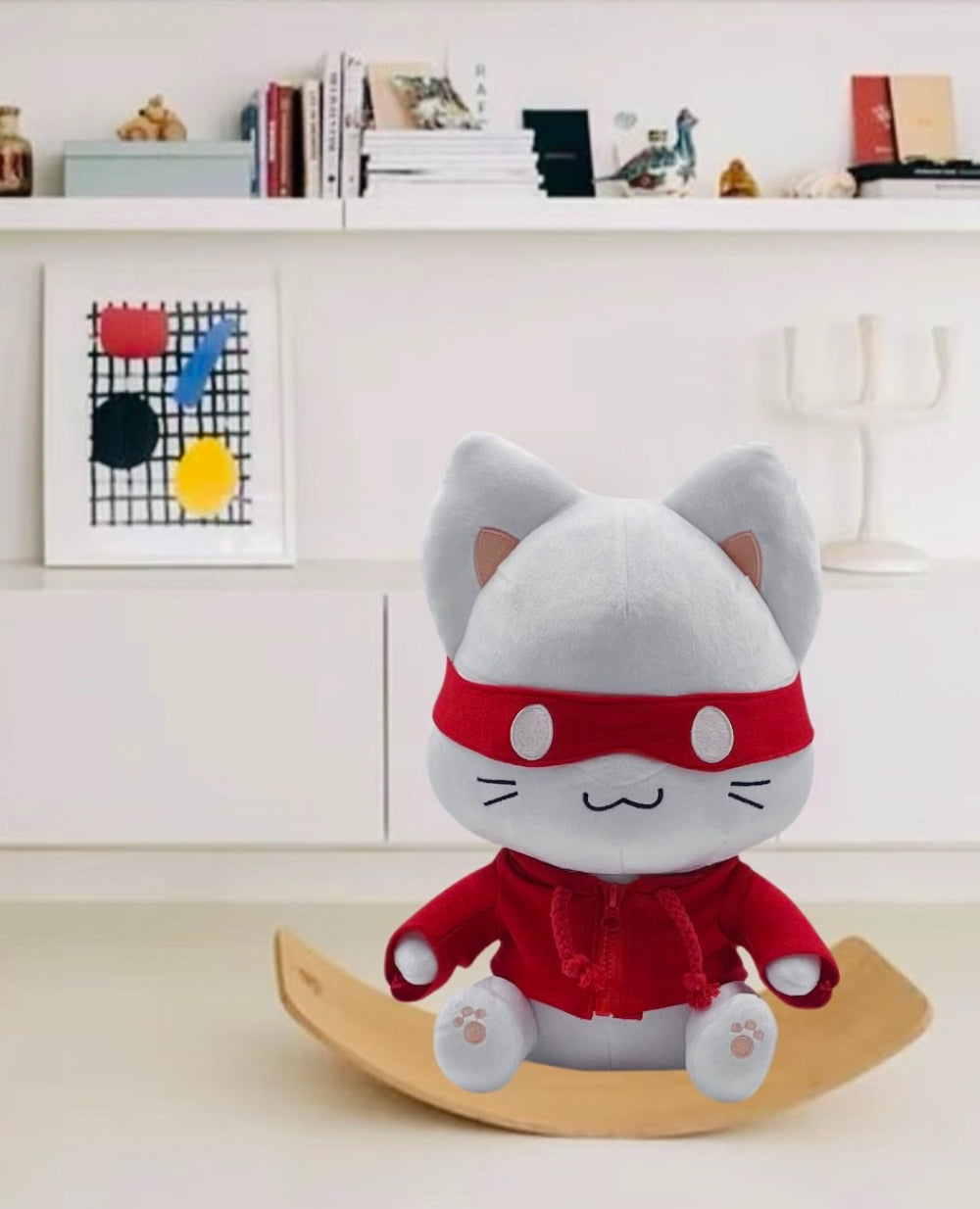 Plush toy cat in a red outfit on a wooden stand with a white shelf in the background