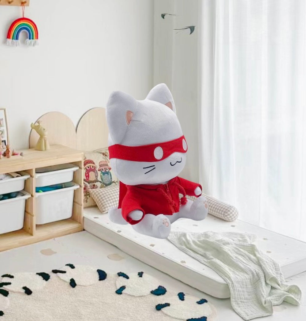 Plush toy cat in a red outfit on a bed in a child's room with toys and a rainbow decoration.