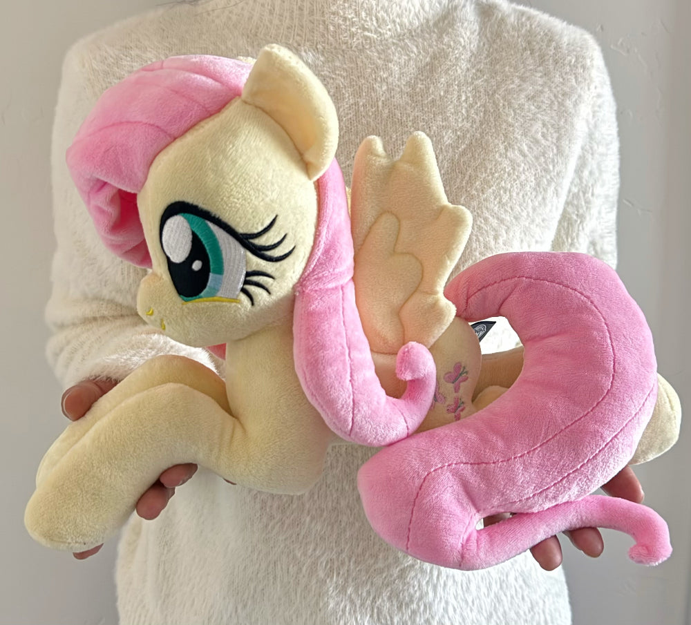 Plush toy of a dragon with pink mane and tail held by a person wearing a white robe.