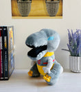 Load image into Gallery viewer, Plush toy resembling a robot dinosaur on a shelf with books and a plant in the background