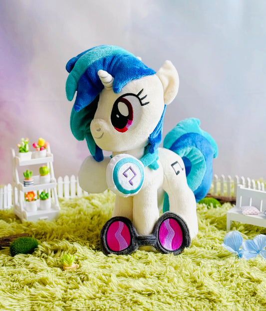 Plush toy resembling a character with blue hair and pink eyes on a green surface.
