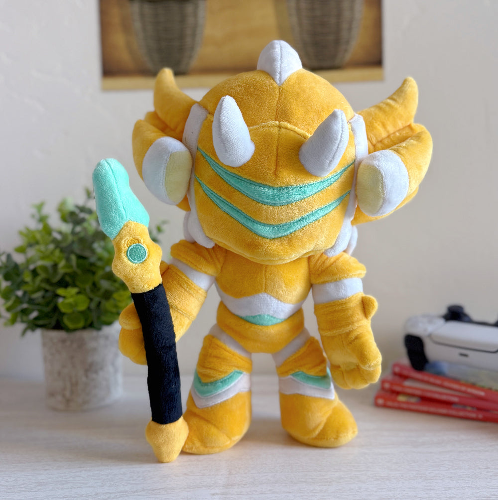 Yellow plush toy with white accents holding a sword on a surface with a plant and books in the background.