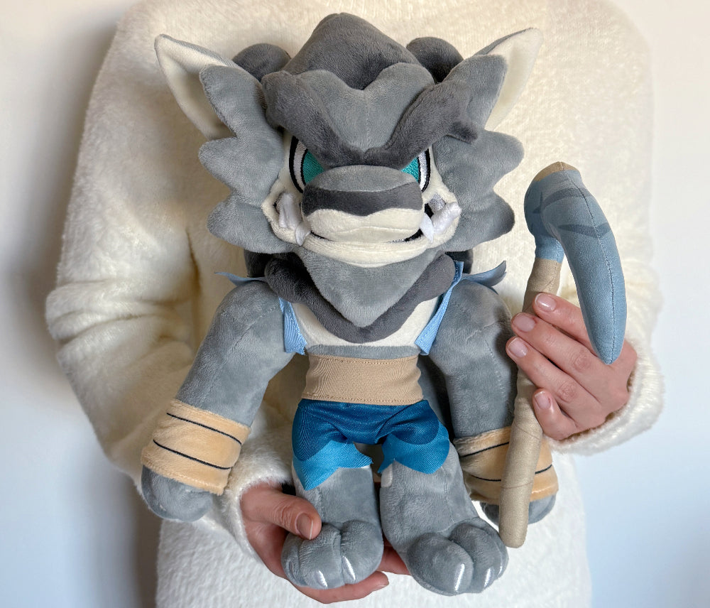 Plush toy of a gray and blue creature held by a person against a white background