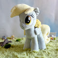 Load image into Gallery viewer, Plush toy of a pony with a yellow hat and flower on a grassy surface