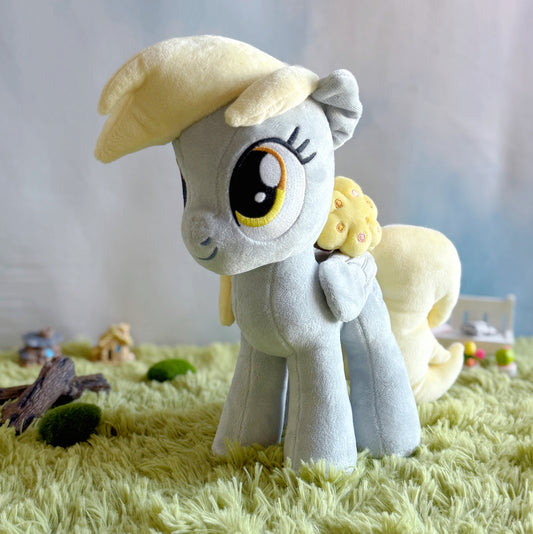 Plush toy of a pony with a yellow hat and flower on a grassy surface