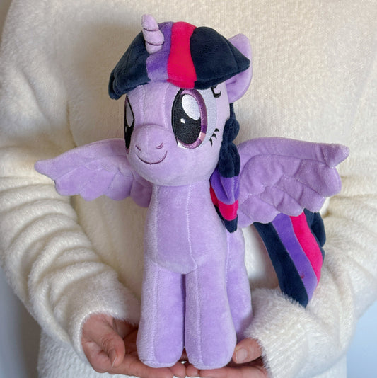 Plush toy of a purple dragon with a colorful hat held by a person against a white background