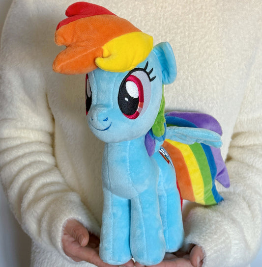 Plush toy of a rainbow-colored pony held by a person against a white background