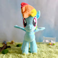 Load image into Gallery viewer, Plush toy of a character with a rainbow-colored mane on a grassy surface.