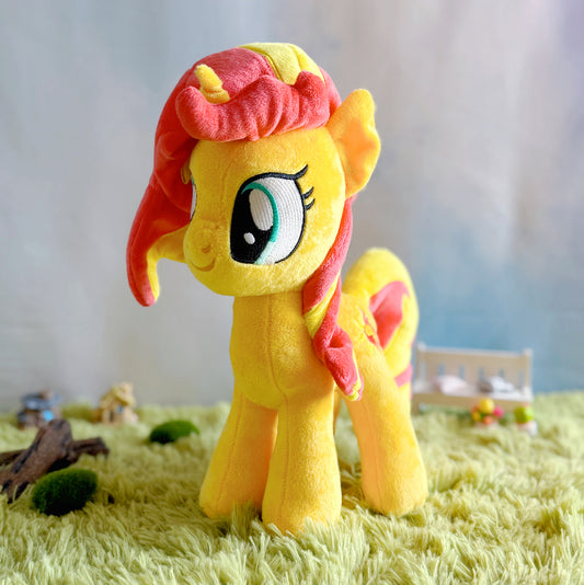 Plush toy of a yellow pony with red hair on a grass-like surface