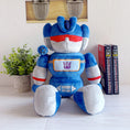 Load image into Gallery viewer, Blue and white robot plush toy with a Transformers logo on a light surface.
