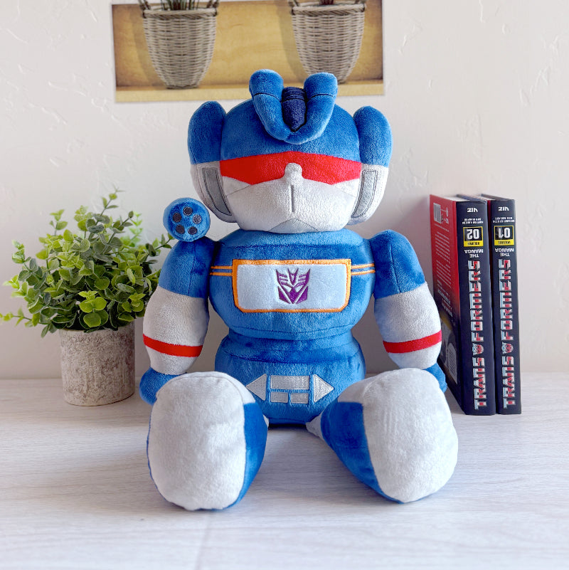 Blue and white robot plush toy with a Transformers logo on a light surface.