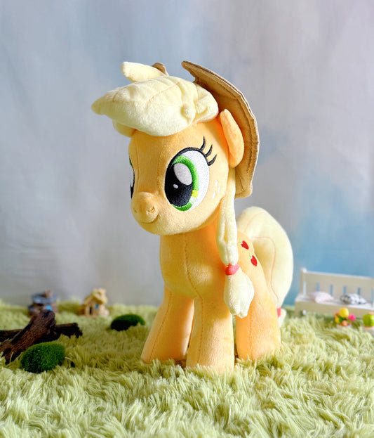 Plush toy of a yellow pony with a hat on a grassy surface