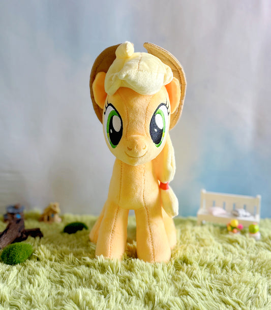 Plush toy resembling a yellow pony with a white mane on a grassy surface with a blurred background
