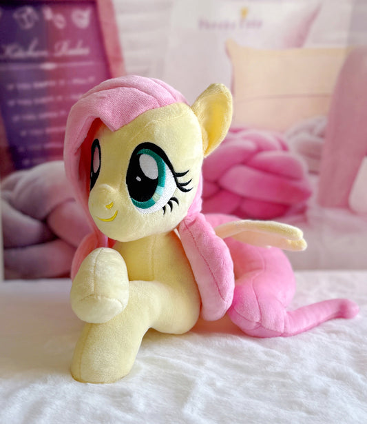 Plush toy resembling a cartoon character with pink hair and wings on a white surface.