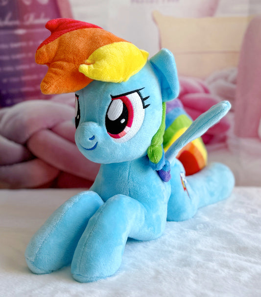 Plush toy of a blue pony with a rainbow-colored mane on a soft surface.