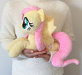 Load image into Gallery viewer, Plush toy of a pink-haired pony held by a person wearing a white sweater.