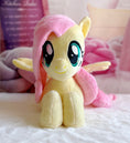 Load image into Gallery viewer, Plush toy resembling a character with pink hair and wings on a soft surface