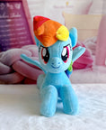 Load image into Gallery viewer, Plush toy resembling a character with a rainbow-colored mane on a soft surface.
