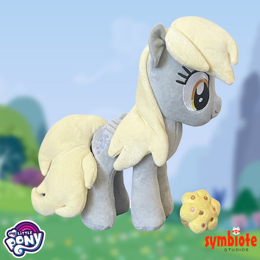 Plush toy of a gray pony with blonde mane and tail, holding a cookie, against a blurred outdoor background.