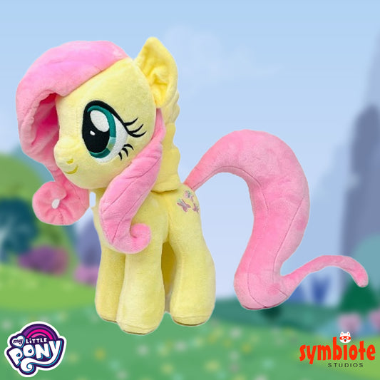 Plush toy of a yellow pony with pink hair and tail against a blurred outdoor background