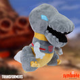 Load image into Gallery viewer, Plush toy of a dinosaur-like character with a Transformers logo on a blurred background
