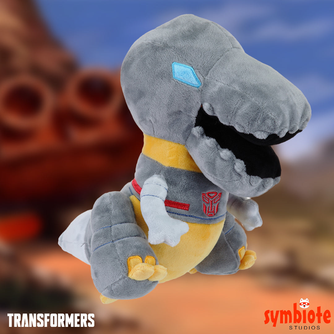 Plush toy of a dinosaur-like character with a Transformers logo on a blurred background