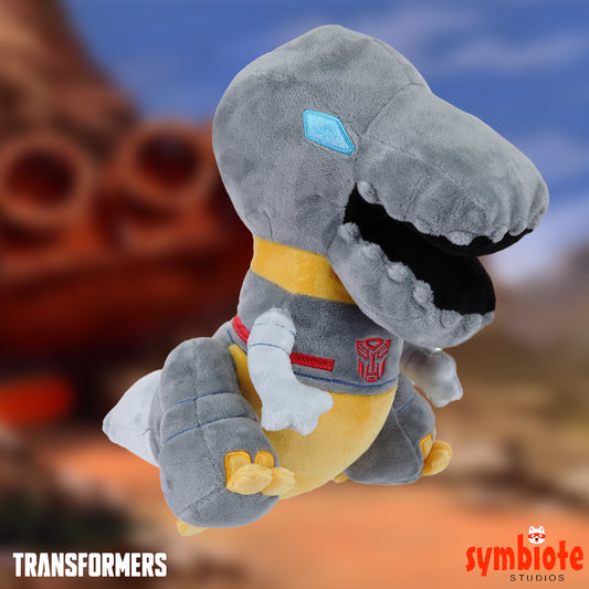 Plush toy of a dinosaur-like character with a Transformers logo on a blurred background