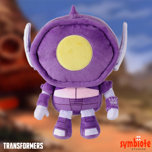 Purple plush toy with yellow circle on a blurred background, featuring 'Transformers' branding.