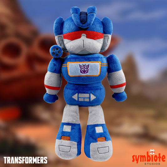 Blue robot plush toy with red and white accents against a blurred natural background