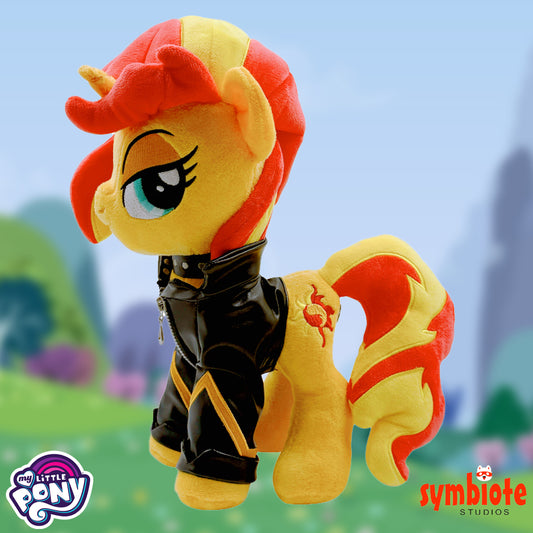 Plush toy of a pony character with red and yellow hair, wearing a black leather outfit, against a blurred outdoor background.