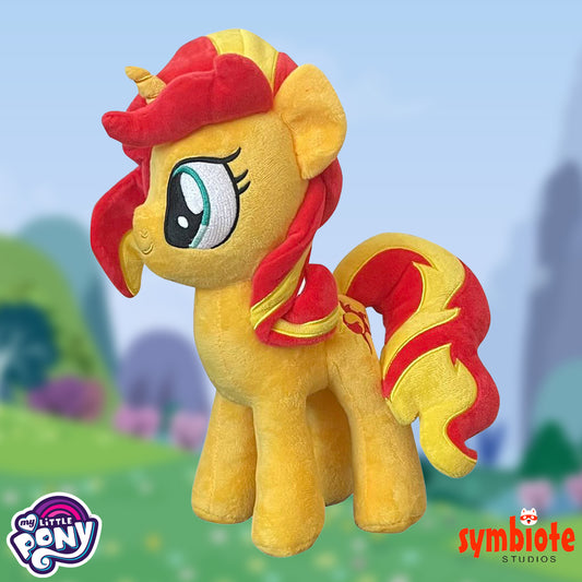 Plush toy of a yellow pony with red mane and tail against a blurred outdoor background