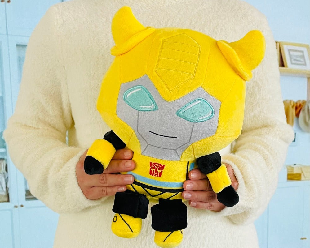 Person holding a yellow and gray plush toy with a Transformers logo.