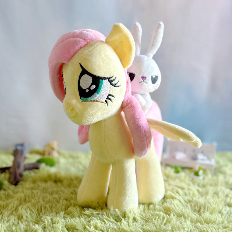 Plush toy of a yellow pony with pink hair on a green surface