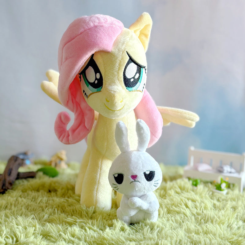 Plush toy of a yellow pony with pink hair and a white rabbit plush toy on a grass-like surface.